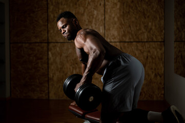 Fototapeta na wymiar African american man with naked torso doing triceps row with dumbbell on bench. 