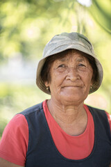Naklejka na ściany i meble Close-up portrait of a pensive elderly woman in a panama hat in a summer garden.