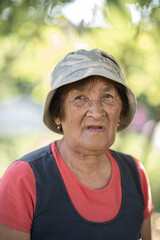 Naklejka na ściany i meble Close-up portrait of a pensive elderly woman in a panama hat in a summer garden.
