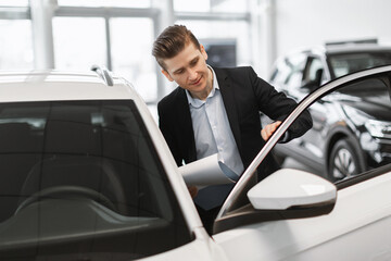 Handsome young car salesman checking automobile before selling at dealership center