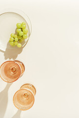 Two glasses of white wine from pale pink colored glass with hard shadows from sunlight and plate with grape fruit, creative summer drink minimal concept, modern glass