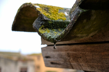 Last drops of rainwater falling from a roof. A drop is seen falling from a rustic roof with a wooden beam.