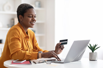 Happy young black businesswoman using laptop, holding credit card