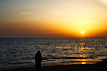 young girl standing on the beach watching the sunset