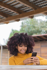 Fototapeta na wymiar Young Afro woman texting on her cell phone. Concept of young afro American girl outdoors checking chats on her device.