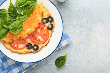 Omelette with tomatoes, black olives, cottage cheese and green spinach herbs on white plate on grey concrete background. Delicious breakfast. Healthy breakfast food. Top view.
