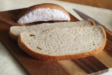Sliced bread lies on a wooden board. There is a knife next to it. farm product