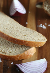 Sliced bread lies on a wooden board. There is an onion nearby. Salt is scattered on the board.