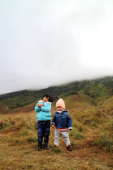 Fototapeta na wymiar two asian toddler show their action standing on the mountain using their jacket