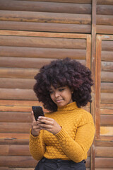 Young Afro woman texting on her cell phone. Concept of young afro American girl outdoors checking chats on her device.