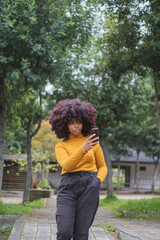Fototapeta premium Young Afro woman texting on her cell phone. Concept of young afro American girl outdoors checking chats on her device.