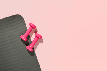 Stylish gray and pink fitness training and gym flat lay. Top view of gray sport mat and pink dumbbells on pink background. Set for pilates, fitness with copy space