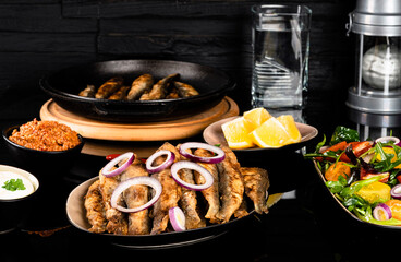 Fried herring fish with lemon, salad, and sauce.