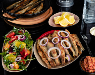 Fried herring fish with lemon, salad, and sauce.