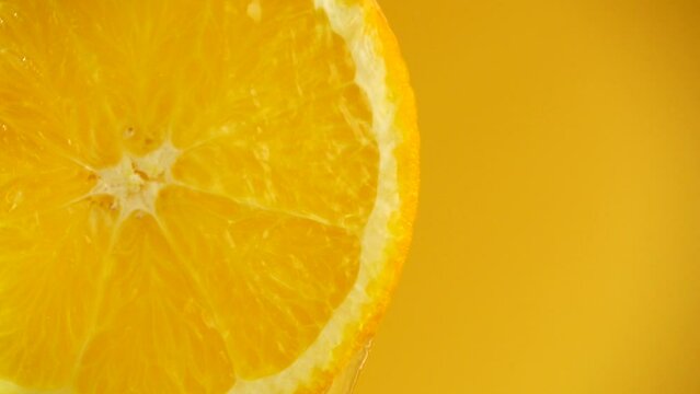 Water flows down from an orange slice on an orange background. Slow motion.