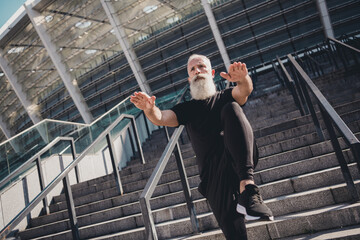 Photo of confident pretty man pensioner dressed black clothes warming up before training outdoors city street