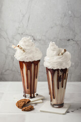 Milkshakes with chocolate with whipped cream, cookies in a tall glass on a light background. Selective focus. vertical position. Delicious dessert drink.