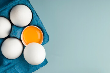Chicken fresh eggs in eco-packaging on a blue background. Broken egg with yolk in the shell. Farm natural products. Top view. Copy space