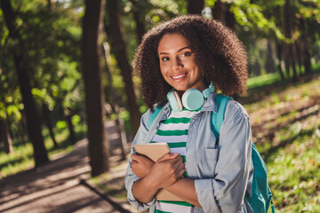 Photo of youth attractive cheerful african lady green trees academic material courses earphones...