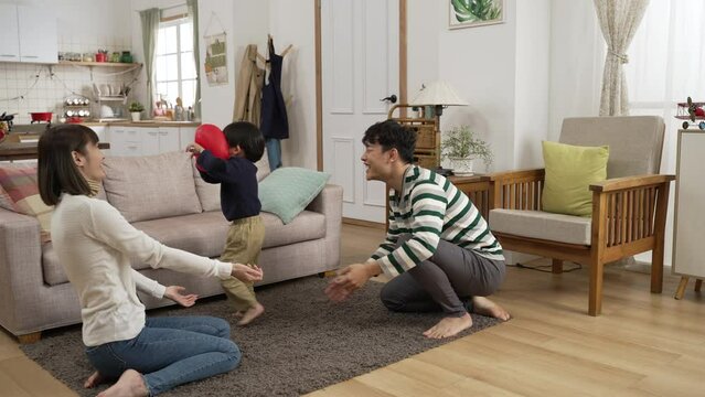 slow motion of cheerful asian dad, mom and preschool son enjoying playing together with a red balloon at home. they hit and catch the red balloon to prevent it from falling on floor