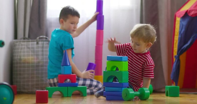 Kids are playing with children building blocks on floor. Building a tower of cubes. Educational toys for children
