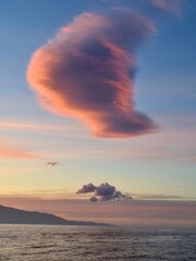 Lonely cloud over the sea in rays of setting sun over the mountains of the island