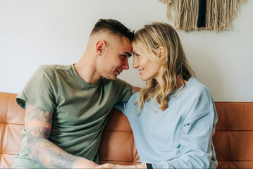 Close-up portrait of a young tattooed man and woman coming together in an embrace at home.