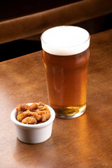 Craft beer pint with pork rinds on wooden table