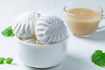 Vanilla Marshmallow dessert zephyr with cup of tea and milk on the table. Meringue dessert with green mint in a white bowl on the white background. traditional Russian sweet dessert. copy space.