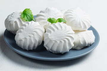 white meringue on a plate.Vanilla Marshmallow dessert zephyr on the table. Meringue dessert with green mint in a grew plate on the white background. traditional Russian sweet dessert. copy space