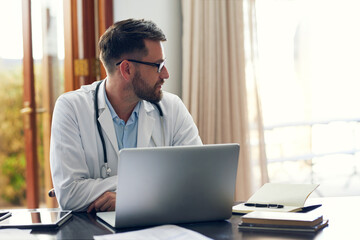 Fototapeta premium Theres a lot of unseen work that doctors do. Cropped shot of a handsome male doctor working on his laptop while sitting in his office.