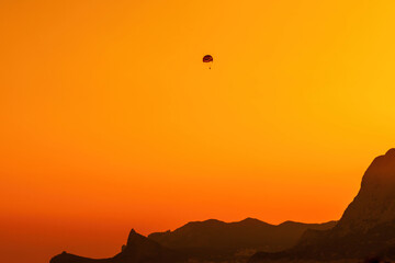 Silhouette of a paraglider soaring over the mountains and the sea at sunset. Extreme sports.