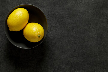 Lemons whole two pieces in black bowl on dark background, top view, space to copy text.