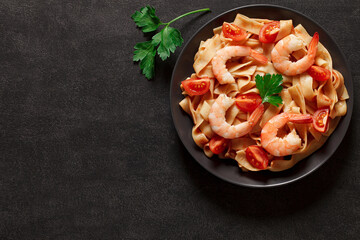 Fettuccine pasta with shrimp and tomato sauce on dark background, top view, space to copy text.