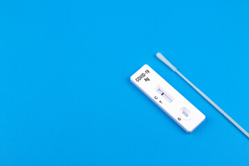 Covid-19 rapid antigen test cassette with nasal swab stick on blue background.