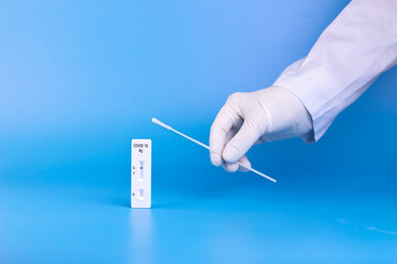 Doctor hand holding Covid -19 rapid antigen test cassette and nasal test stick on blue background.