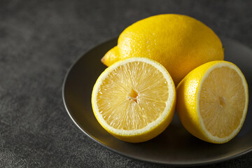 Lemons whole and cut, on dark plate background, selective focus.