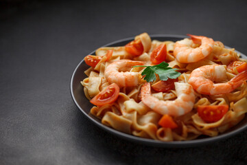 Fettuccine cooked with shrimp and tomatoes on plate, on dark background, selective focus.