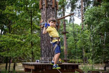 Strong excited young boy playing outdoors in rope park. Caucasian child dressed in casual clothes and sneakers at warm sunny day. Active leisure time with children concept