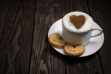 hot drink coffee or tea with whipped cream with heart shaped cookies and decor on dark wooden background with copy space