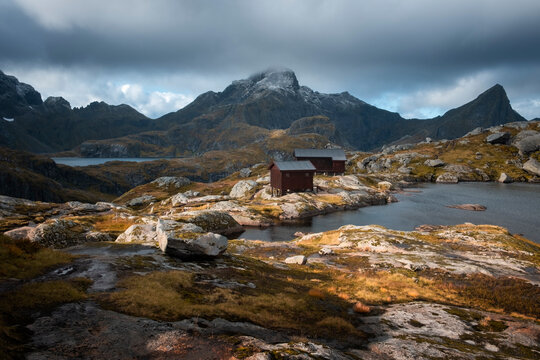 Autumn mountain landscape. Lofoten Islands Norway. Manken mountain hike, wooden houses, shelter and lake under sunlight against a stormy sky