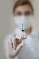 Woman in medical uniform and mask with injection syringe in hand. Virus and vaccination concept. Doctor or nurse at work. Close-up, selective focus.