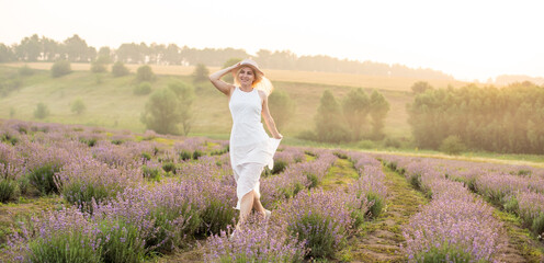 Beautiful young woman wearing a white dress walking in the middle of a lavender field in bloom