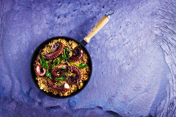 A portion of risotto with octopus tentacles. purple background. Top view