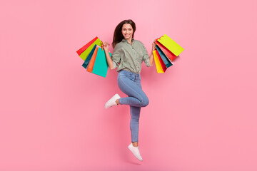Photo of excited lucky woman wear striped shirt rising shopping bags jumping high isolated pink color background
