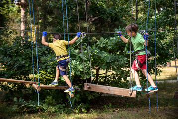 Two strong excited young friends playing outdoors in rope park. Caucasian boys dressed in casual clothes and sneakers at warm sunny day. Active leisure time with children concept