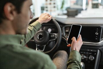 Unrecognizable young man using smartphone, sitting in drivers seat of new car, buying vehicle at auto dealership, mockup