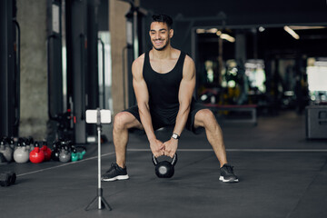 Fototapeta na wymiar Middle Eastern Male Athlete Capturing Online Workouts At Gym For Fitness Blog