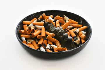 An image of a black ashtray full of dirty old cigarette butts on a white background. 