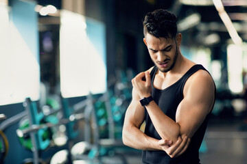 Sport Injuries. Upset Arab Male Athlete Rubbing Injured Elbow While Standing At Gym